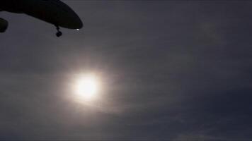 Airplane landing during golden hour creating dramatic silhouettes against vibrant sunset sky, showcasing luminous clouds and backlit aircraft details in slow motion sequence video