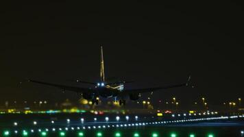 Passenger airplane descending on brightly illuminated runway during nighttime, capturing sequential landing approach from front and below perspective video