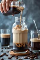 A hand pours coffee into a jar with ice, creating a layered drink against a textured background. photo