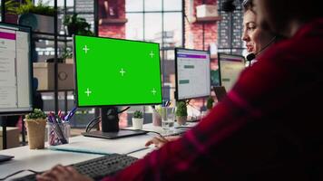 Call center employee working on green screen mockup PC, doing account management in office. Customer support agent in front of chroma key isolated screen computer handling calls, camera B close up video