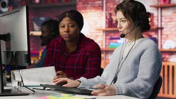 Call center team leader going over paperwork files next to colleague at PC desk. Customer support manager explaining company documentation to intern accommodating with job, camera A video