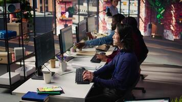 Multiethnic team of call center agents answering clients technical inquiries about hardware issue. Multiracial customer support workers in office doing job using PC to troubleshoot problems, camera B video