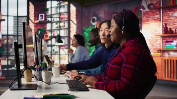 Experienced call center team leader assisting employee and drinking coffee in office. Asian account manager doing teamwork with colleague, enjoying beverage in workplace, camera B video