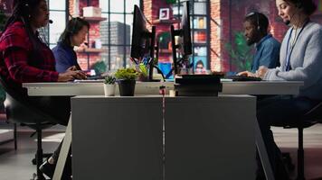 Call center worker speaking in audio headset microphone, using remote access tools. Woman in customer center assisting clients with installing software, communicating through headphones mic, camera B video