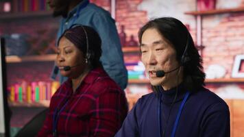 Customer center employee gesturing loud Asian senior agent to quiet down while working African american woman working in call center worker upset by noises in office made by colleague, camera A video