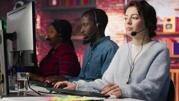 Teamworking call center coworkers in office helping customers by answering questions. Team of agents in customer support workplace in front of PC using headset mic to talk with clients, camera A video