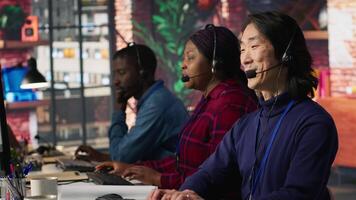 Multiethnic team of call center agents answering clients technical inquiries about hardware issue. Multiracial customer support workers in office doing job using PC to troubleshoot problems, camera A video