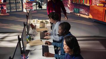 Team of multiethnic call center agents in workplace helping customers. Multiracial workers in diverse customer center assisting clients needing help resetting password, camera B video