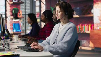 Call center team of agents wearing headset assisting customers over phone at modern workstation with multiple monitors, emphasizing customer support, communication and service efficiency, camera A video