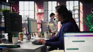Technical support specialist in call center office troubleshooting customer connectivity issue through step by step guidance using headset and computer workstation, camera B video