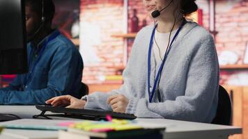 Call center worker speaking in audio headset microphone, using remote access tools. Woman in customer center assisting clients with installing software, communicating through headphones mic, camera A video