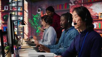 Call center operator next to coworkers dealing with upset customers, speaking using headset at office desk. Teamworking staff members doing customer support job, handling clients complaints, camera B video