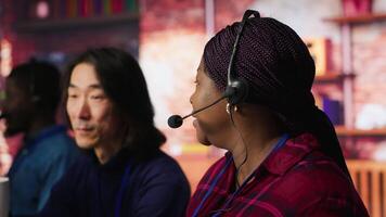 Experienced call center team leader assisting employee and drinking coffee in office. Asian account manager doing teamwork with colleague, enjoying beverage in workplace, camera A video