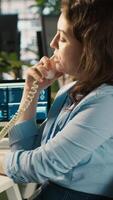 Vertical Worker in office using landline phone to talk with client while reviewing charts. Employee at work discussing with business partner during call, analyzing business performance metrics, camera A video