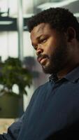 Vertical Worker in office reviewing financial graphs, analyzing business performance metrics. African american employee at work looking over data trends and strategic insights, camera B video
