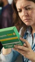 Vertical Stressed woman in office feeling painful headache while working, suffering burnout, reading medication box instructions. Employee having migraine after working overtime to finish project, camera A video