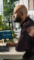 Vertical Arab office clerk working to hit key performance targets for revenue, profitability and operational efficiency. Middle Eastern employee at PC desk doing research analysis, camera A video