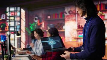 Call center worker arriving at work, using artificial intelligence on laptop to enhance customer interactions. Asian senior agent entering customer service office, using AI technology, camera B video