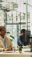 Vertical Accountant in busy modern startup agency imputing financial figures on PC after checking reports. Focused businesswoman working in modern office, crosschecking data, camera B video