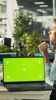 Vertical Green screen laptop on office desk next to employee editing documents on computer. Mockup notebook next to worker analyzing data charts, interpreting statistical information, camera B video