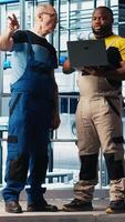 Vertical Senior engineer talking with intern in smart factory, collecting and analyzing data. Experienced technician helping trainee use tracking software in industrial plant equipped with sensors, camera A video