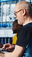 Vertical Smart factory expert using laptop software to test automated systems and ensure reliability. Worker uses program on notebook to identify bottlenecks and optimize gear based on sensors data, camera A video