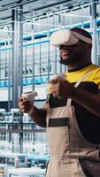 Vertical Smart factory engineer using VR headset to oversee operation of robotic arms and conveyor belts. Industry 4.0 plant technician monitors system performance using virtual reality, camera A video