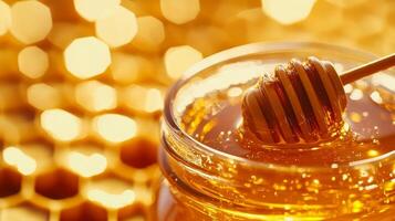 Golden honey dripping from wooden dipper into glass jar with honeycomb background photo