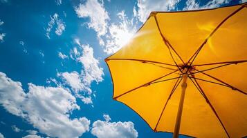 Bright sunlight shining through yellow umbrella against blue sky with fluffy clouds photo