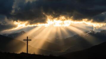 Sunlight streaming through clouds over mountainous landscape with cross silhouette photo
