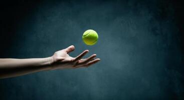 Caucasian adult hand tossing tennis ball against dark background photo