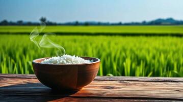 A bowl of rice on a wooden table in front of a rice field photo