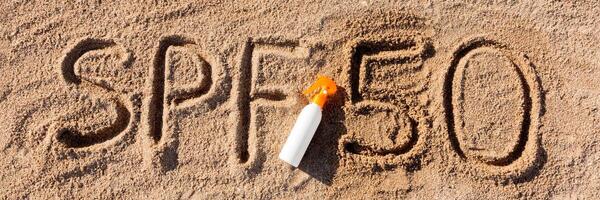 Sun protect factor fifty. SPF 50 word written the sand and white bottle with suntan cream. Skin care concept background photo