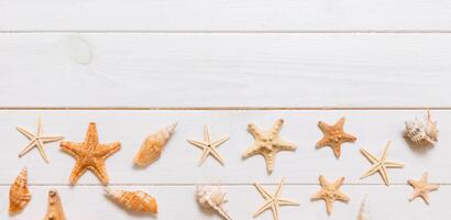 Summertime wooden table with starfish and seashells on a white background banner top view. Copy space background, summer concept photo