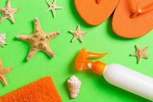 Top view Beach flat lay accessories. sunscreen bottle with seashells, starfish, towel and flip-flop Colored background copy space photo