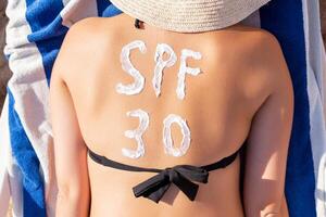 Spf 30 word is drawn with sunblock on woman's back lying on the sunbed at the beach. Sun protection factor concept photo