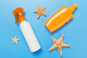 sunscreen cream with starfish and seashells bottles on blue background, top view photo
