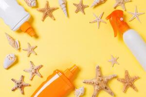 sunscreen cream with starfish and seashells in bottles yellow background, top view photo