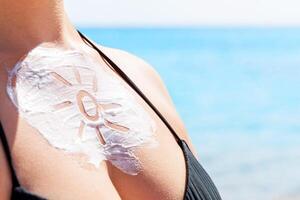 Sun shaped sunscreen woman's breast over sea background photo