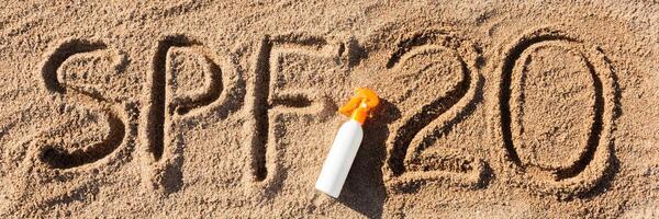 Sun protect factor twenty SPF 20 word written on the sand and white bottle with suntan cream. Skin care concept background photo