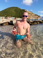 Smiling man holding starfish in clear tropical sea on sunny beach photo