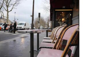 Rainy Paris street with empty wicker cafe chairs and table outside a bistro photo