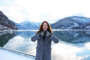Joyful woman making heart symbol by snowy fjord in Gaupne, Norway winter scenery photo