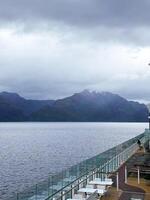 Cruise Ship Deck Overlooks Calm Fjord and Snowy Mountain Under Cloudy Sky photo