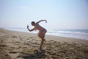 Dancer in motion on wide sandy beach under bright sky near ocean waves photo