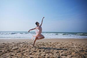 Dancer in mid-leap on sandy beach in flowing dress with ocean in background photo