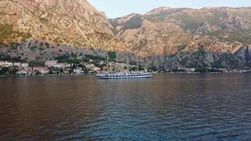 Kotor, Montenegro, 08-27-2024, Sunset landscape of the Royal Clipper sailing ship in the Bay of Kotor in the sea between the mountains. Drone view of used cruise ship travel and holidays video