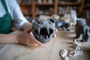 Potter holds saber toothed lion figurine with open jaws, work on custom clay cat series in workshop photo