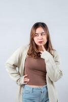young woman in a cozy sweater, with a thoughtful expression, touches her chin while looking to the side against a neutral background photo