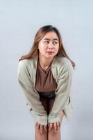 young woman in a cozy sweater leans forward with a curious and playful expression, looking to the side against a neutral background photo